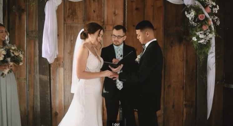 Eric guiding a couple through their vows in a barn with wooden walls and floral draping