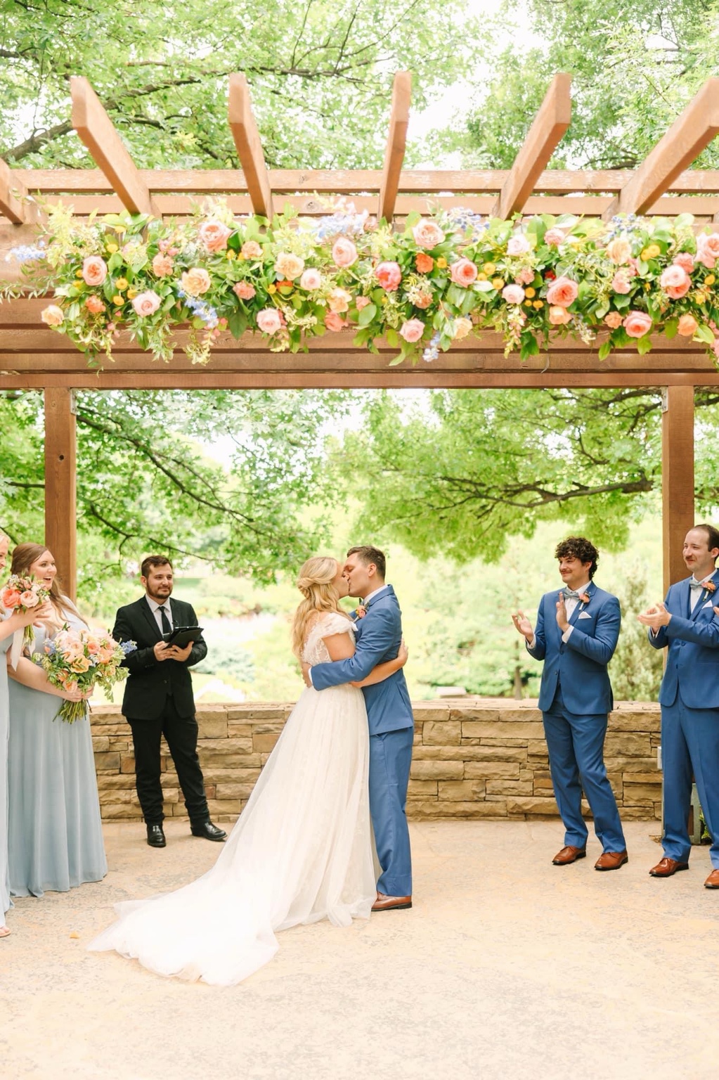 Eric officiating an outdoor wedding beneath a floral pergola as the couple kisses