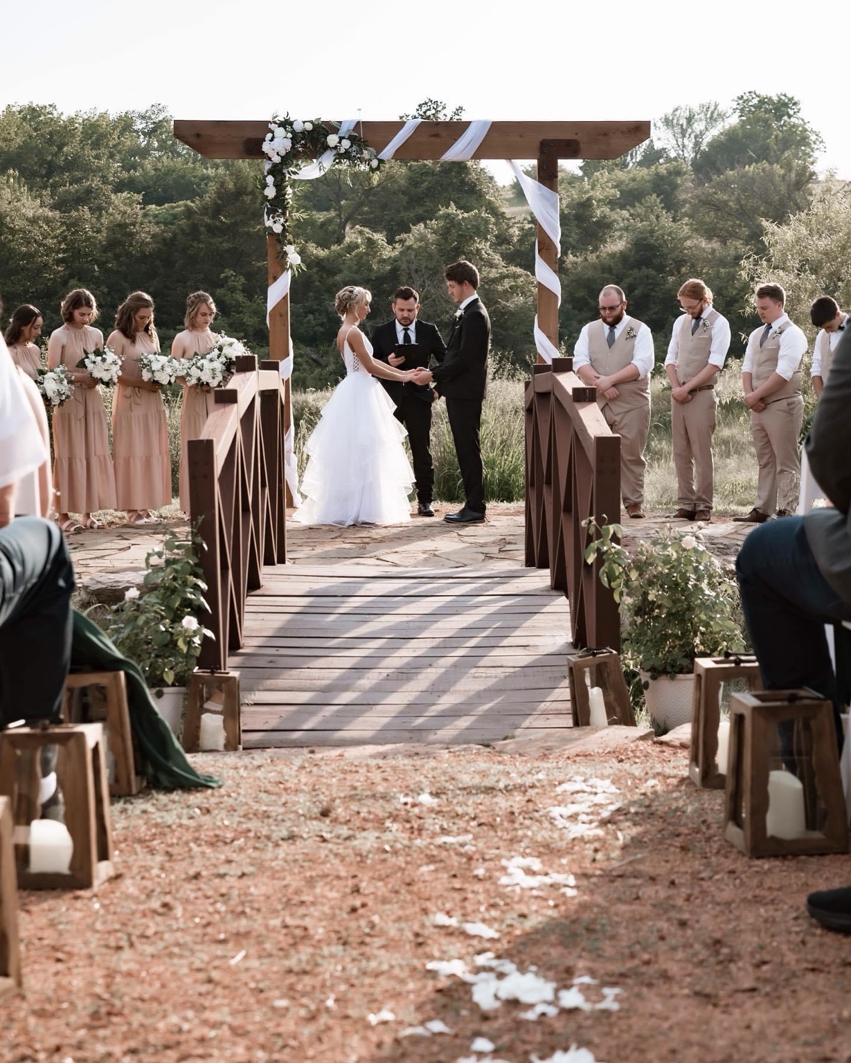 Eric officiating as a couple exchanges vows beneath a flower-covered wooden arch